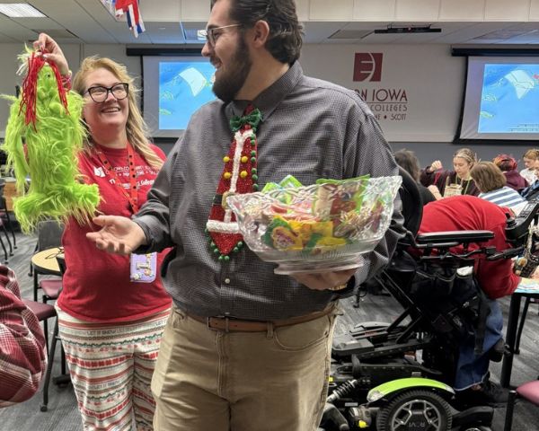 EICC Associate Professor Lori Sheppard holds up a stuffed grinch to a colleague who is holding a bowl of candy during a 2025 holiday craft event for children and families. 