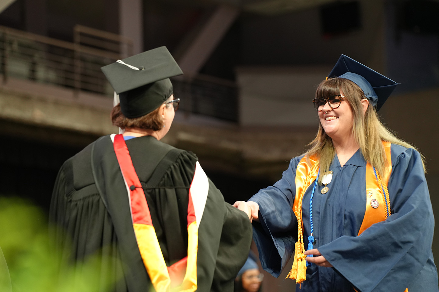 Joeanna Moore smiles as she shakes hands with SCC President Ann Lawler in academic regalia while receiving her diploma on stage during graduation.